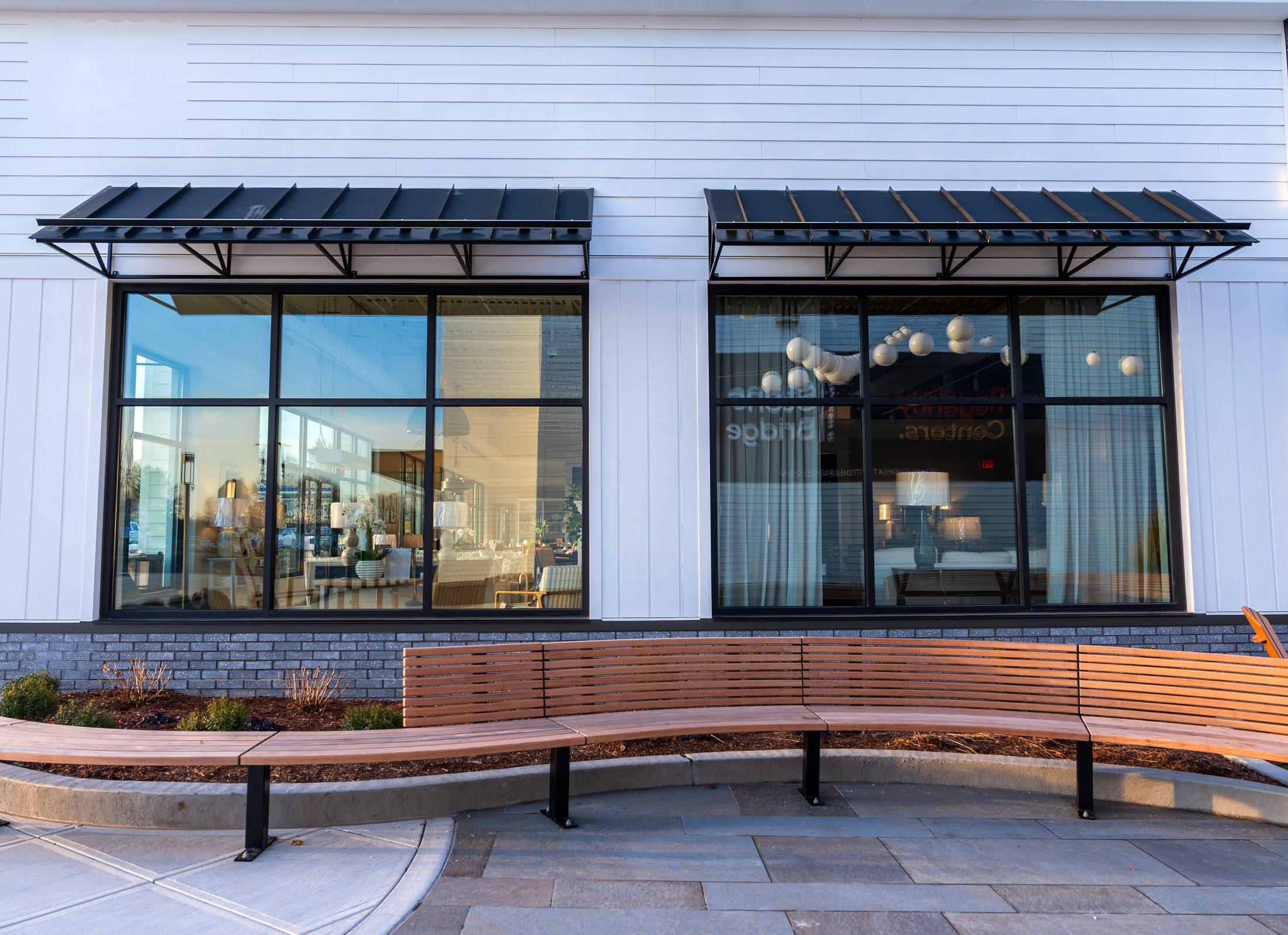 Two black metal window awnings above a curved wood bench by Manchester Awning