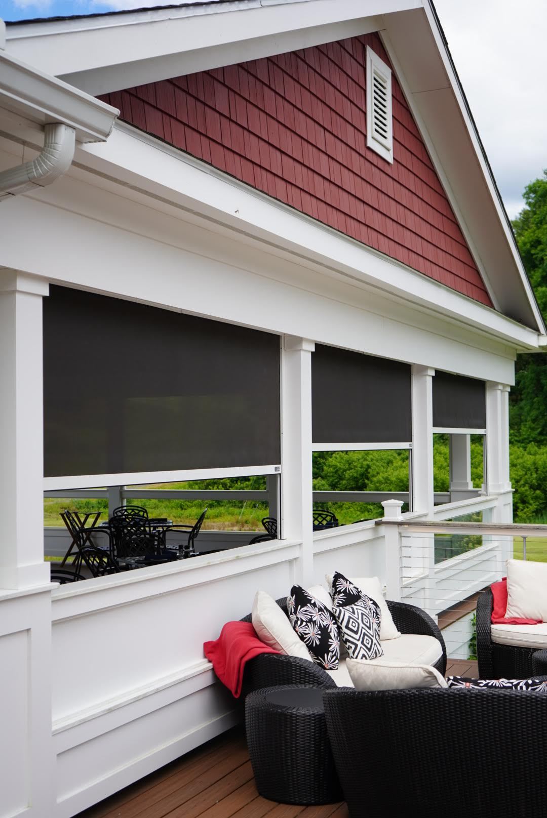 Three Freedom screens lowered between the posts of a covered porch, shading a furnished deck