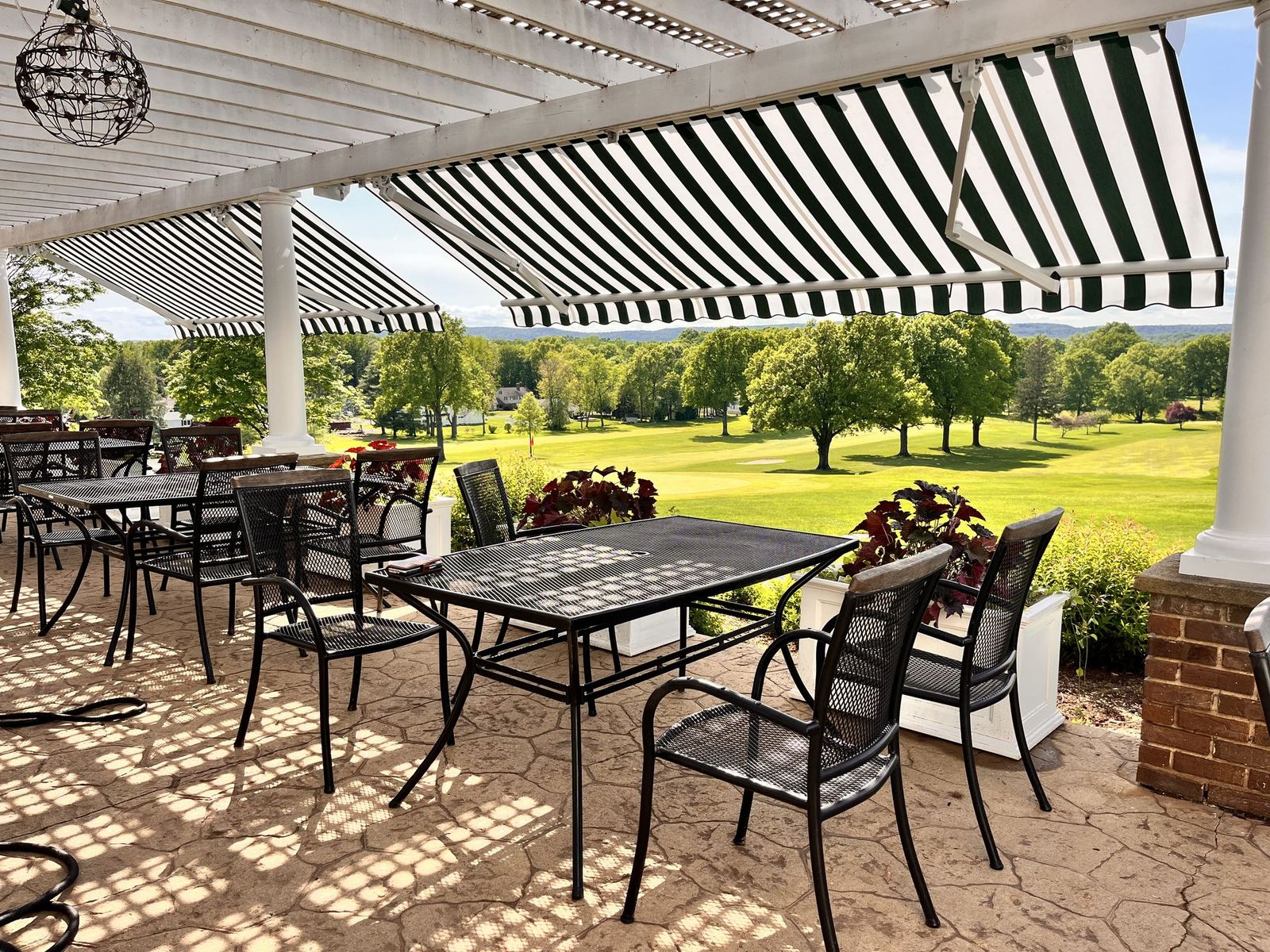 Legend retractable awning seen from beneath, striped acrylic fabric shading a paved patio with dining tables