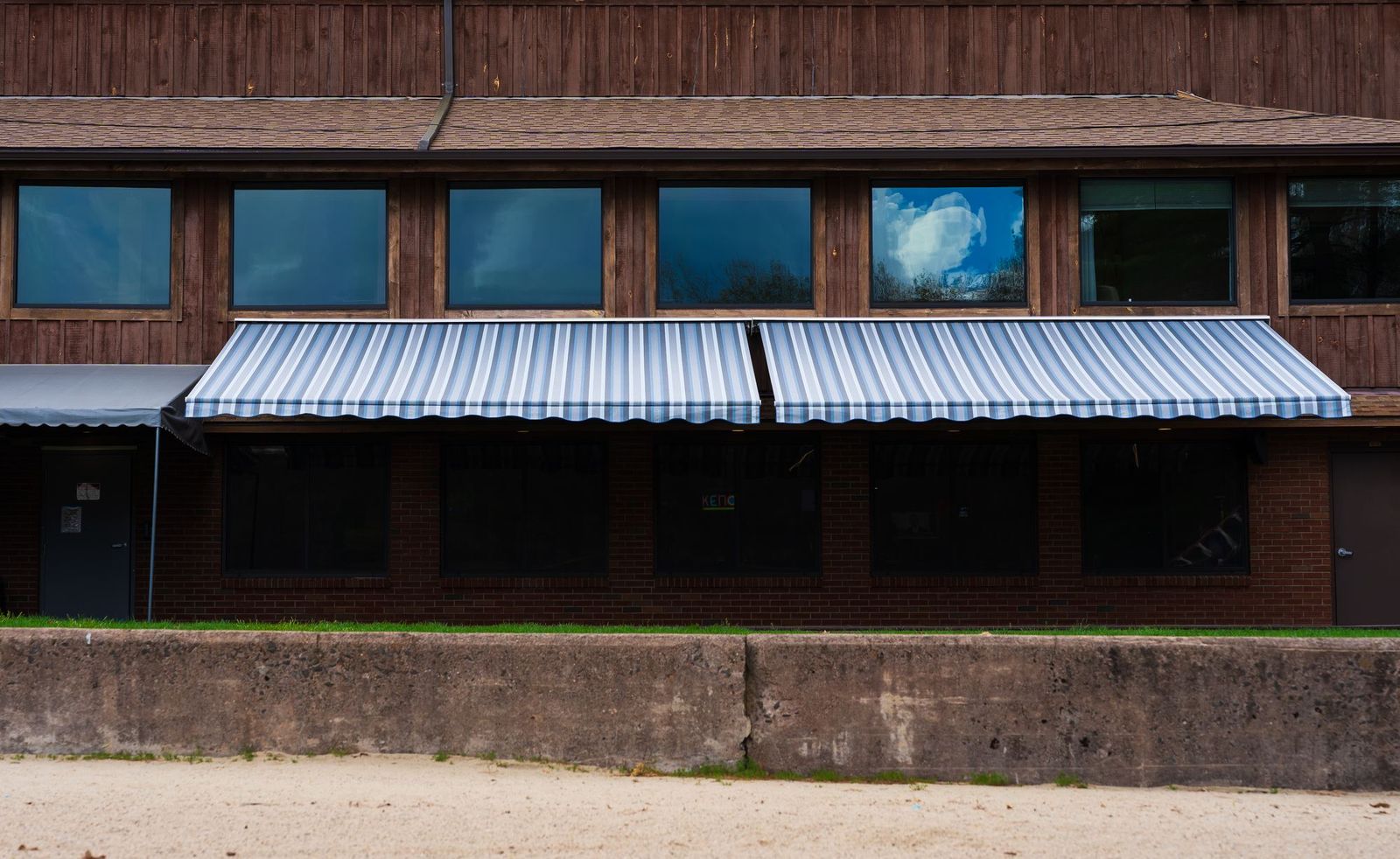 Two large side-by-side striped Liberty retractable awnings extended across the front of a commercial building